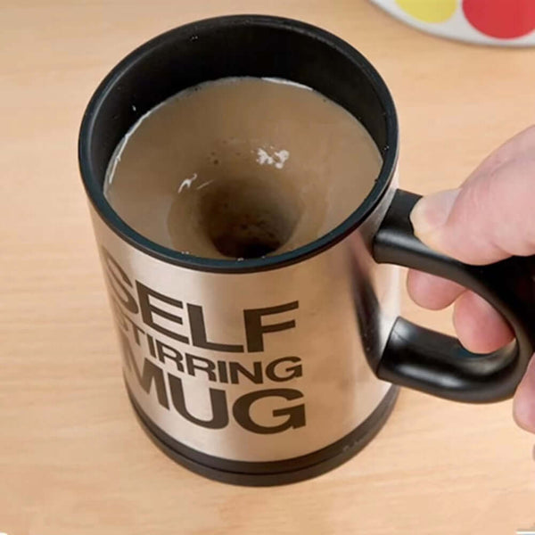Automatic electric self-stirring mug in hand, showing mixed coffee inside, stainless steel design on wooden surface.