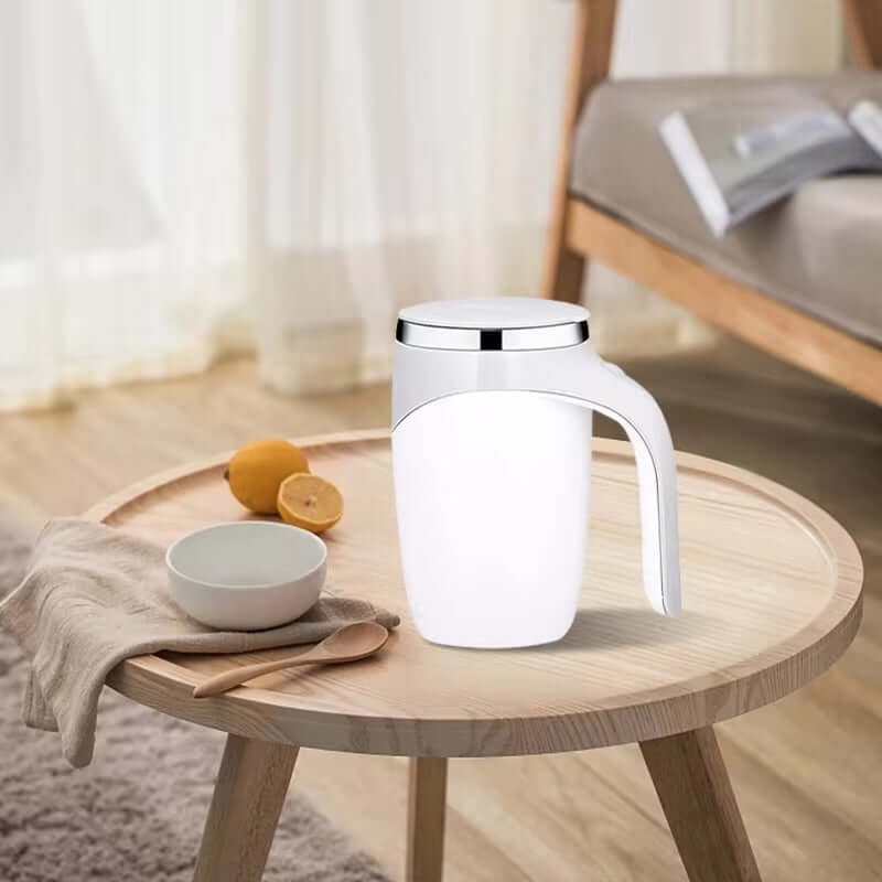 Automatic stirring cup on a wooden table near a bowl and lemon, showcasing its sleek white design.