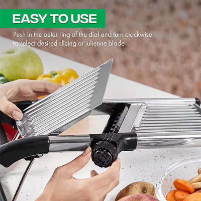Hands adjusting the dial on an adjustable stainless steel mandoline slicer with fresh vegetables in the background.
